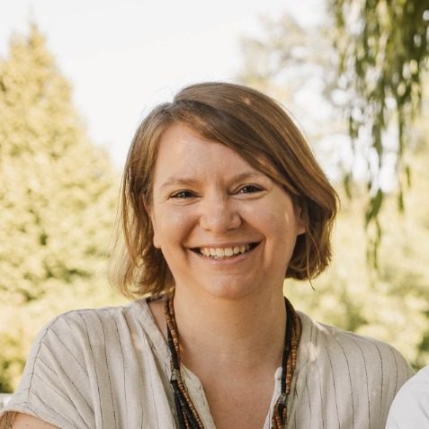 Nadja Daunicht, lächelnd mit kurzen, blonden Haaren und einem hellen Oberteil im Freien.